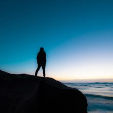 Person standing on cliff looking out to sea